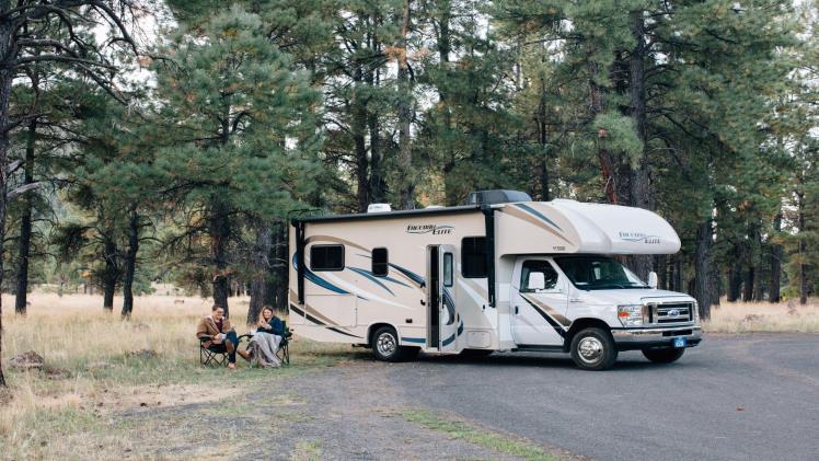 A couple sits in front of their RV in the woods, which Veritas Global Protection can protect